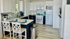 A modern kitchen with white cabinets, a central island with chairs, a coffee maker, a toaster, and a refrigerator.