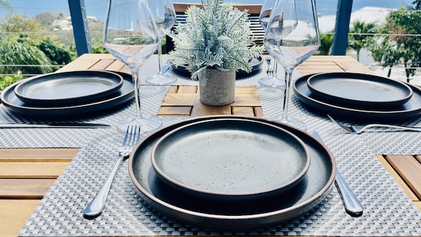 A table set for two with dark plates, clear glasses, and a small potted plant.