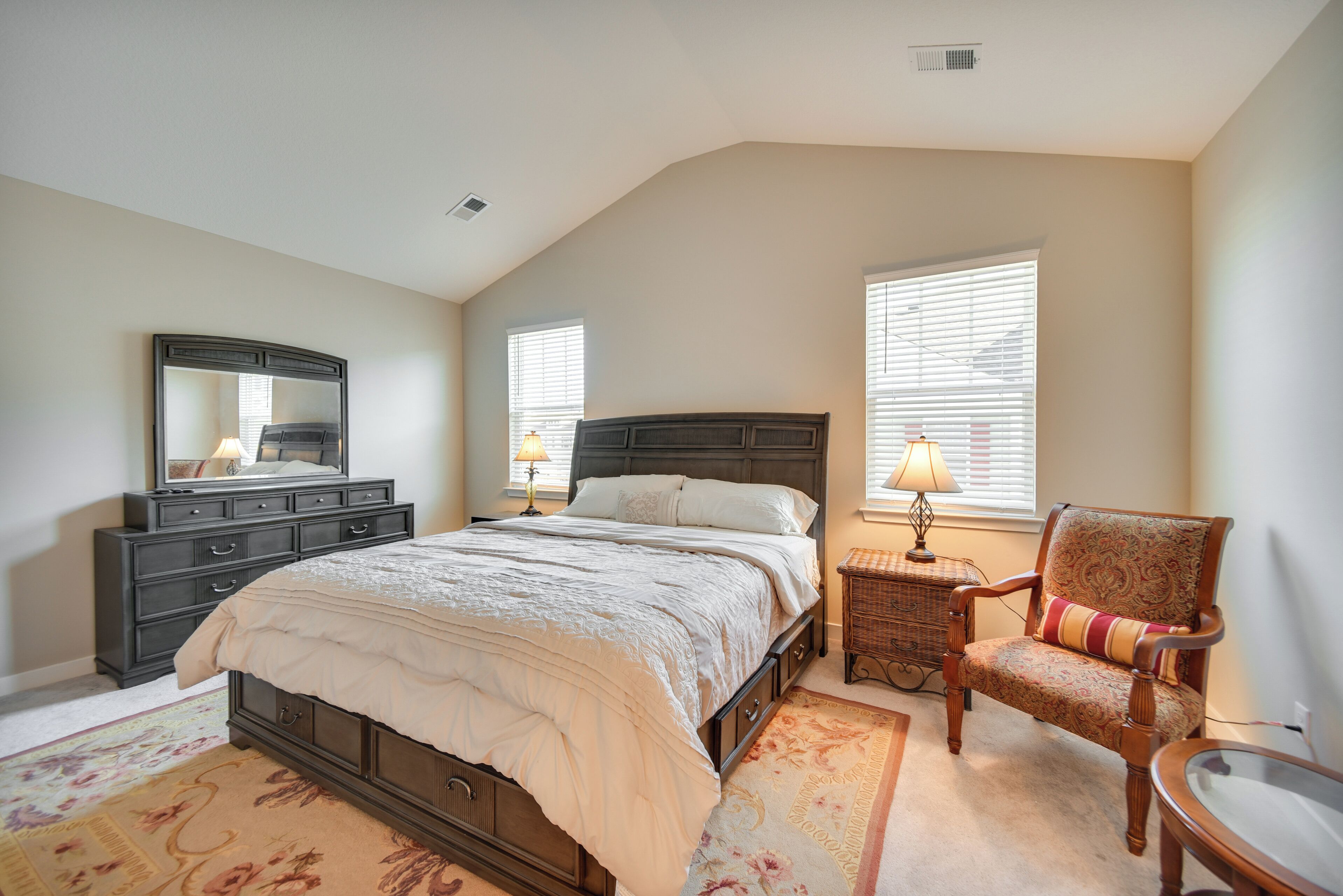 A bedroom with a large bed, a dresser, a chair, and two lamps.
