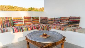 Un espace extérieur aménagé avec des sièges blancs, des coussins colorés à rayures et une table ronde en bois agrémentée d’un objet décoratif.