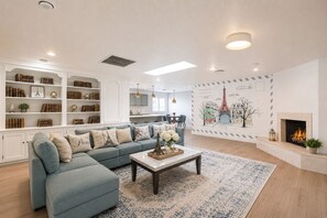 Sala de estar com sofá seccional, mesa de centro, lareira e parede com painel de paisagem urbana.