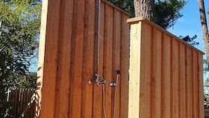 A wooden fence with a metal gate and a showerhead attached to it.