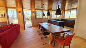 Interior acolhedor de uma cabana com uma mesa de jantar de madeira, cadeiras vermelhas e um sofá vermelho.