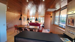 Interior em madeira com área de refeições, sofá vermelho e bancada de cozinha.