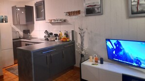 Una cucina moderna con mobili grigi, un'isola centrale e un televisore a schermo piatto su un supporto bianco.