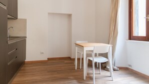 A small, sparsely furnished room with a wooden floor, a white table, and a white chair. - Cozy Studio in the heart of Navigli (Milano)