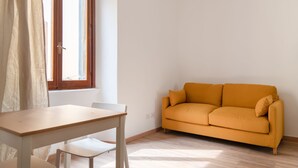 A room with a wooden table and chairs, a mustard-colored sofa, a window with curtains, and a light-colored floor. - Cozy Studio in the heart of Navigli (Milano)