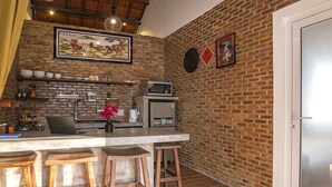 A kitchen with a brick wall, a microwave, a coffee maker, and wooden stools.