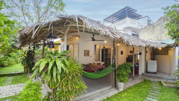 A house with a thatched roof, a dining area, and a small garden with potted plants.
