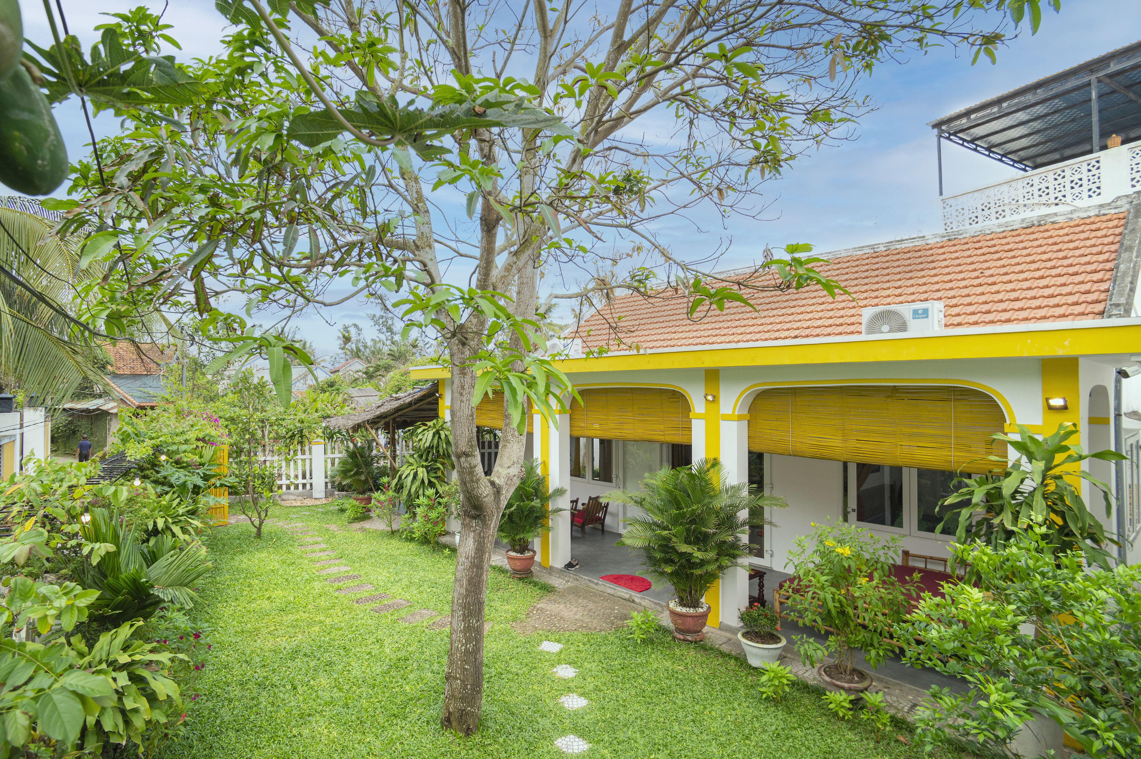 A yellow building with a covered patio and a garden with potted plants.
