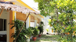 A courtyard with potted plants, a thatched roof structure, and a building with yellow and white walls.