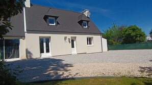 Ein zweistöckiges Haus mit einem Schotterweg, einem grünen Zaun und Bäumen im Hintergrund.