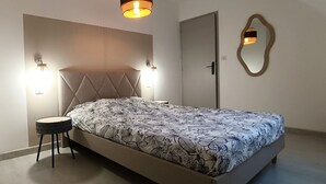 Ein Schlafzimmer mit einem Bett, einem runden Beistelltisch, einem wandmontierten Spiegel und zwei Wandleuchten.