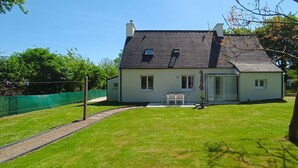 Ein zweistöckiges Haus mit dunklem Dach, einer Veranda und einem kleinen Garten.