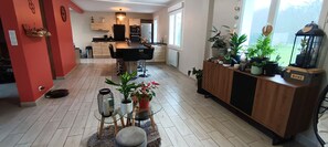 A modern kitchen with a dining area, featuring a glass-top table, potted plants, and a wooden cabinet with a 'HOME' sign. - Cosy family home ideally located. (Crozon)