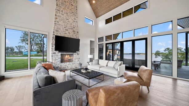 A spacious living room with a stone fireplace, large windows, and a view of a golf course. - Unbelievable lake or golf course views from every room! (Afton)
