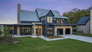 A modern two-story house with a stone facade, large windows, and a covered patio area. - Unbelievable lake or golf course views from every room! (Afton)