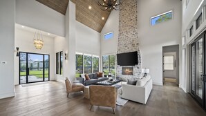 A spacious living room with a stone fireplace, large windows, and a high ceiling. - Unbelievable lake or golf course views from every room! (Afton)