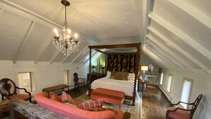 A spacious attic bedroom with a four-poster bed, a wooden bench, and a chandelier.