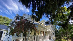 A two-story house with a porch, surrounded by greenery and trees.