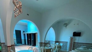 A spacious indoor area with multiple round tables and white chairs, featuring a blue-lit archway leading to an outdoor area. - Selecta Colonial (Villavicencio)