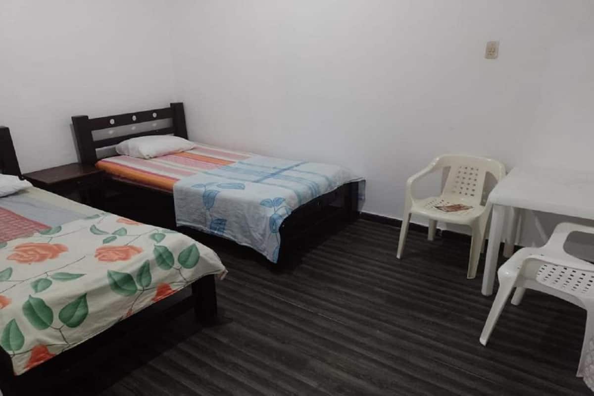 A room with two single beds, a small white table, and two white plastic chairs.