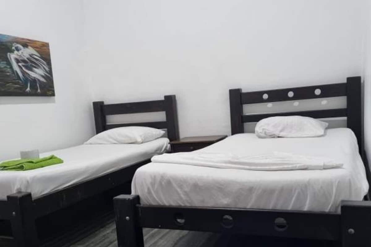 A room with two single beds, each with a wooden headboard and white bedding. There is a green towel on the floor beside one bed.