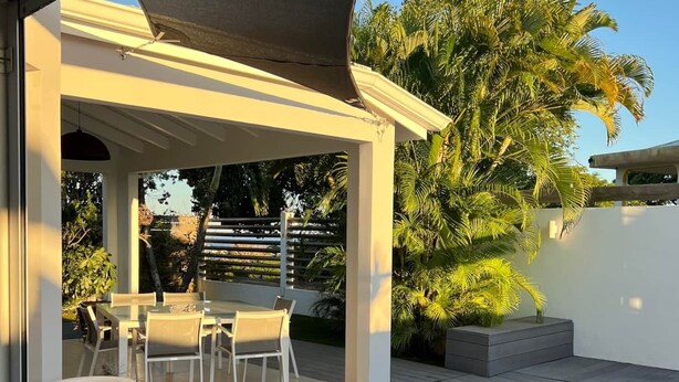 Eine moderne Außenpatio mit Pool, weißen Möbeln und einer überdachten Sitzgelegenheit.