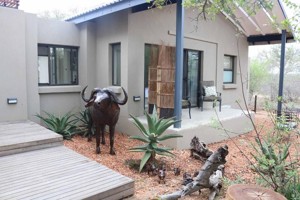 A modern house with a patio, a bull statue, and a thatched structure.