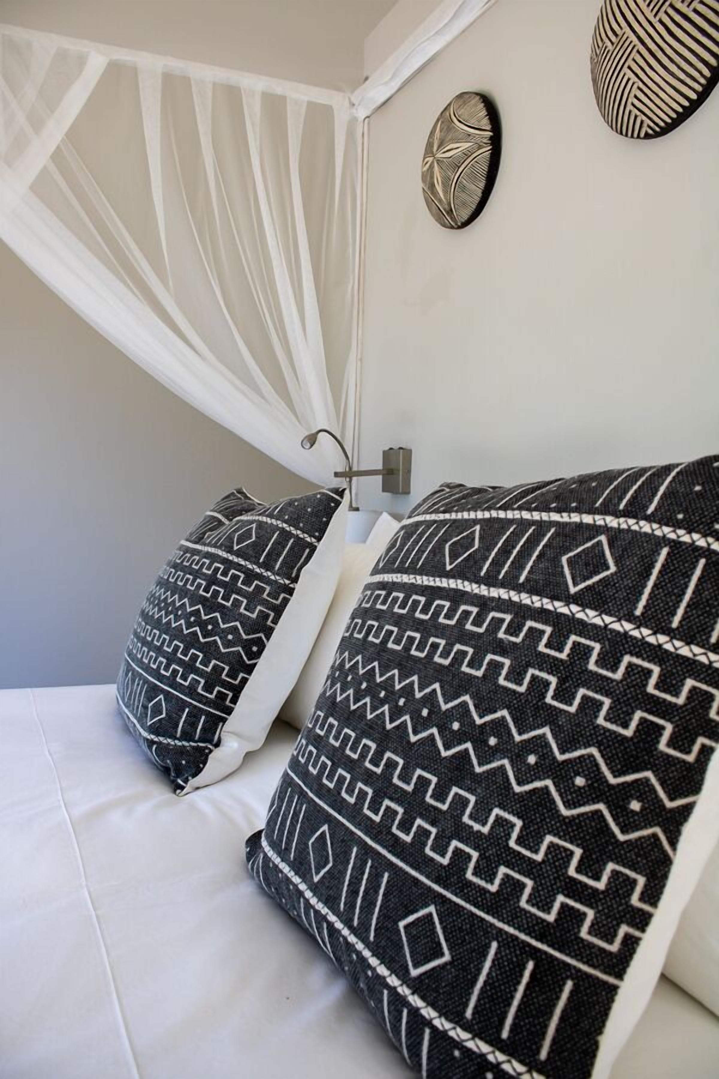 A bed with white bedding and black and white patterned pillows.