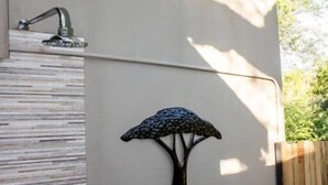 Una dutxa exterior moderna amb teulada de bambú, una ombrel·la fixada a la paret i una tanca de fusta al fons.