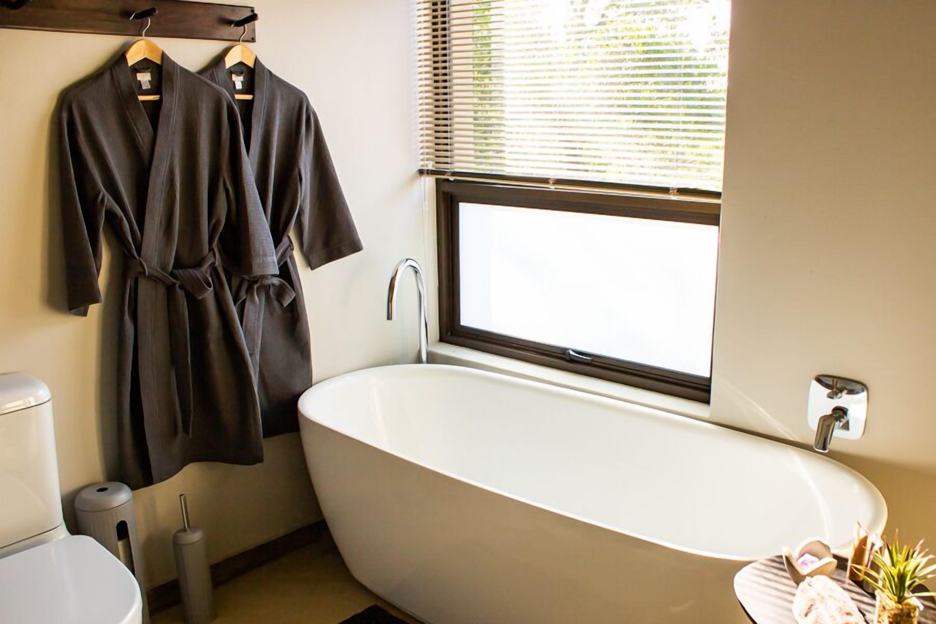 A modern bathroom with a freestanding bathtub, a toilet, and a window with blinds.
