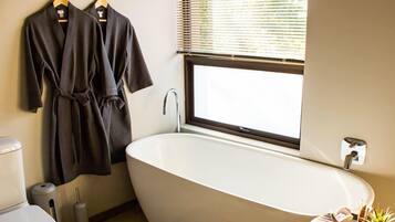 A modern bathroom with a freestanding bathtub, a toilet, and a window with blinds.