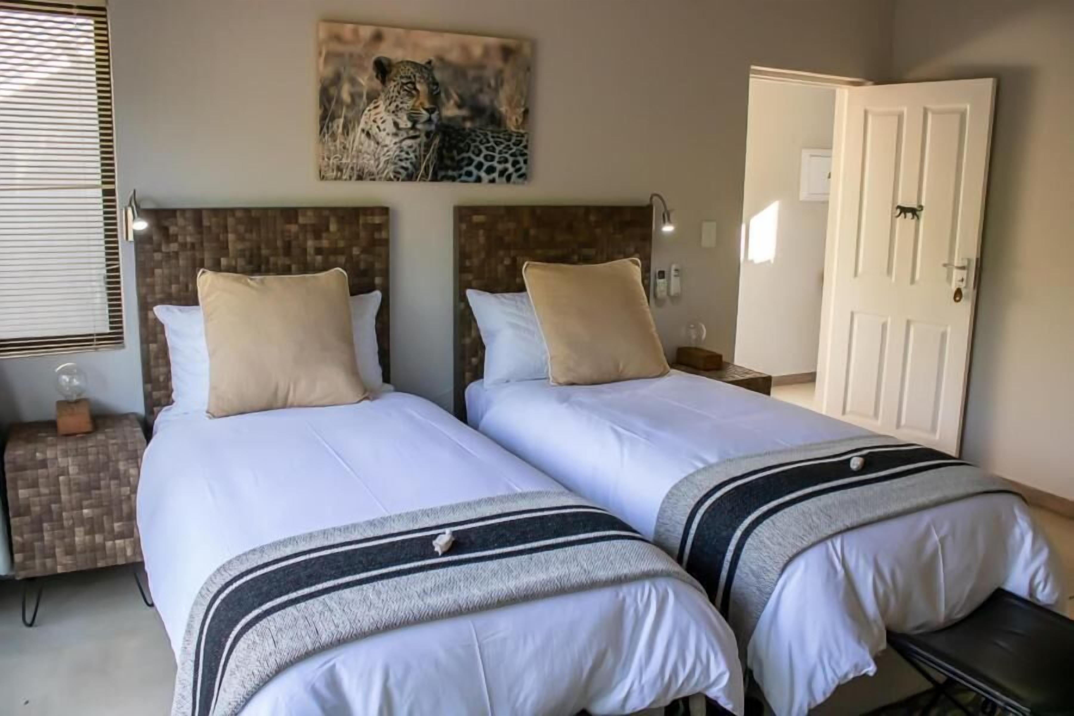A hotel room with two beds, a leopard painting, a door, and a nightstand with a lamp.