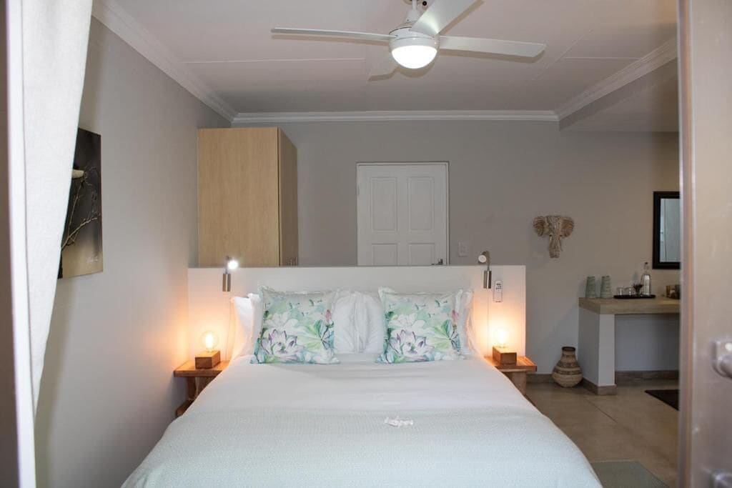 A bedroom with a bed, bedside lamps, a ceiling fan, a door, and a small table with a vase.