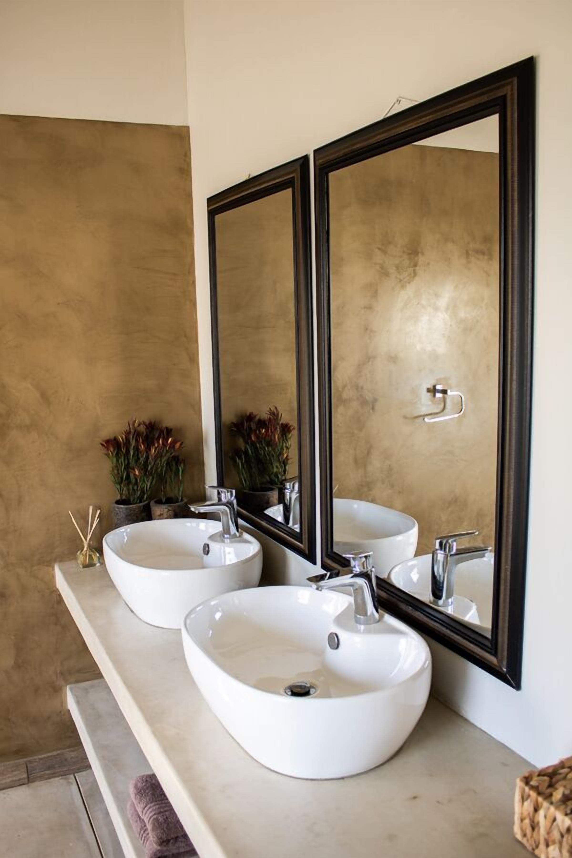 Ein Badezimmer mit zwei weißen Waschbecken, einem großen Spiegel und einer beige ge текстуierten Wand.