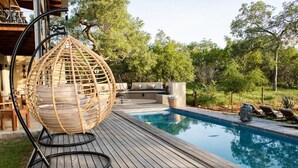Una terrassa de fusta amb una cadira penjant, una piscina i gandules.