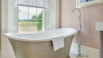 Un baño con una bañera independiente, un ventanal con vistas a un campo y un cuadro en la pared.