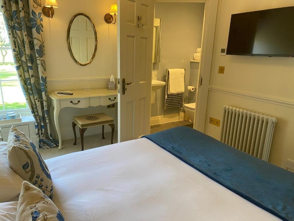 A hotel room with a bed, a vanity with a mirror, a toilet, and a television.