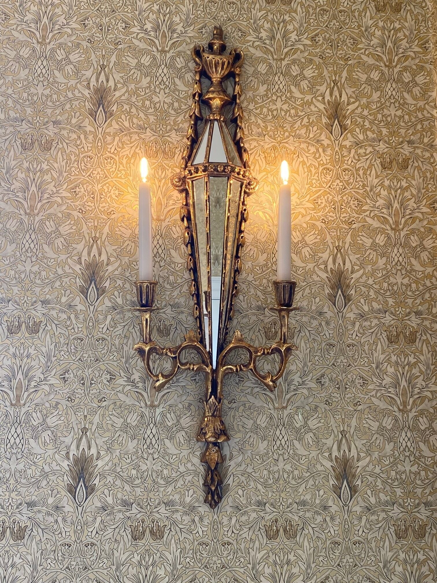Un candelabro de pared con tres velas, sobre un papel tapiz estampado.
