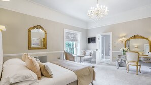 A bedroom with a large bed, a vanity with a mirror, and a chandelier. - Reymerston Hall (Norwich)