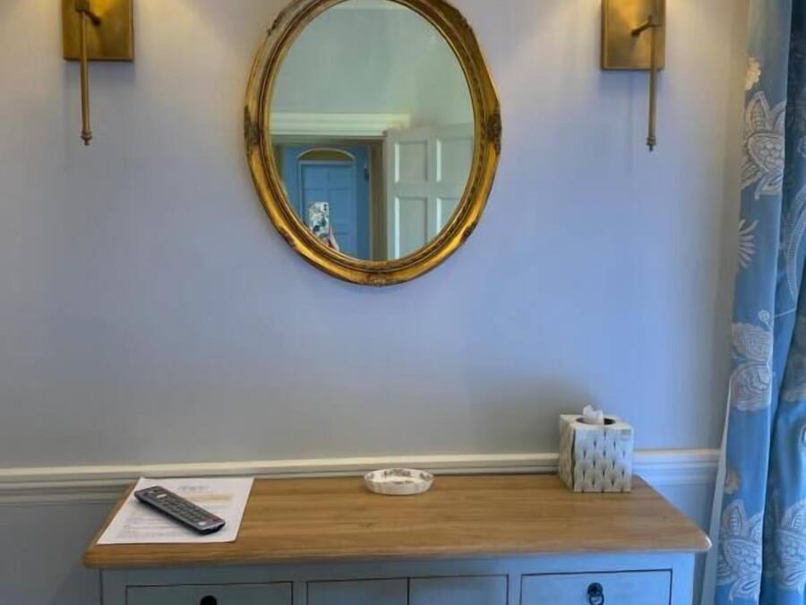 A wooden desk with a round mirror, two wall-mounted lamps, a tissue box, and a remote control on the desk.