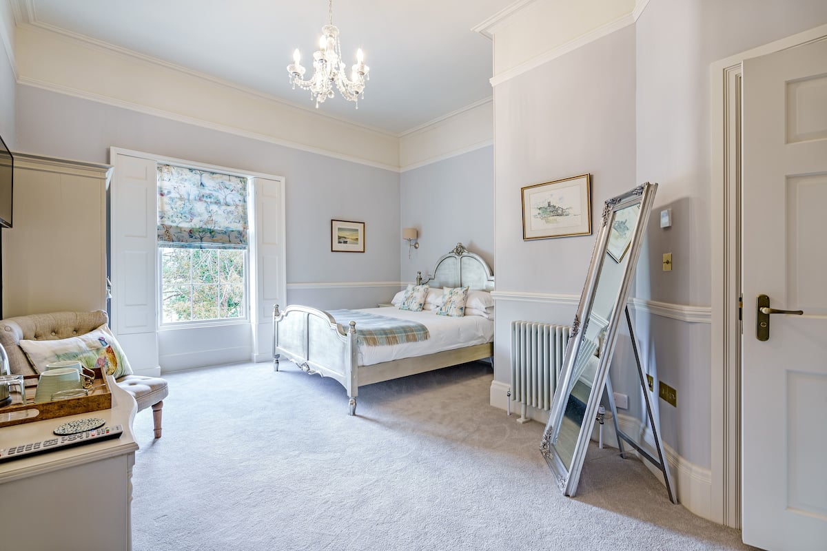 A bedroom with a bed, a dresser, a window with a view, and a chandelier.