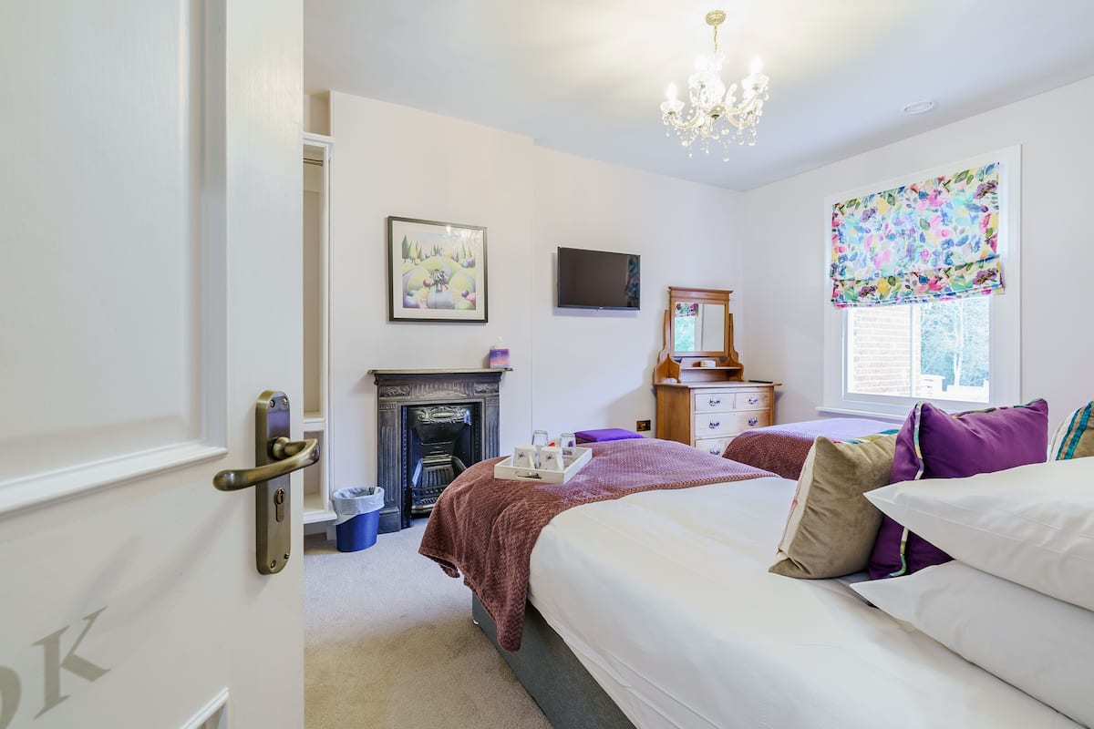 A bedroom with a bed, a dresser, a television, a fireplace, and a window with a floral valance.