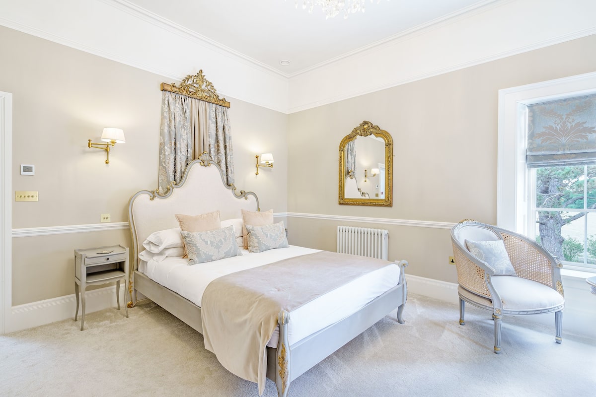 A bedroom with a bed, bedside tables, a chair, a mirror, and a window.