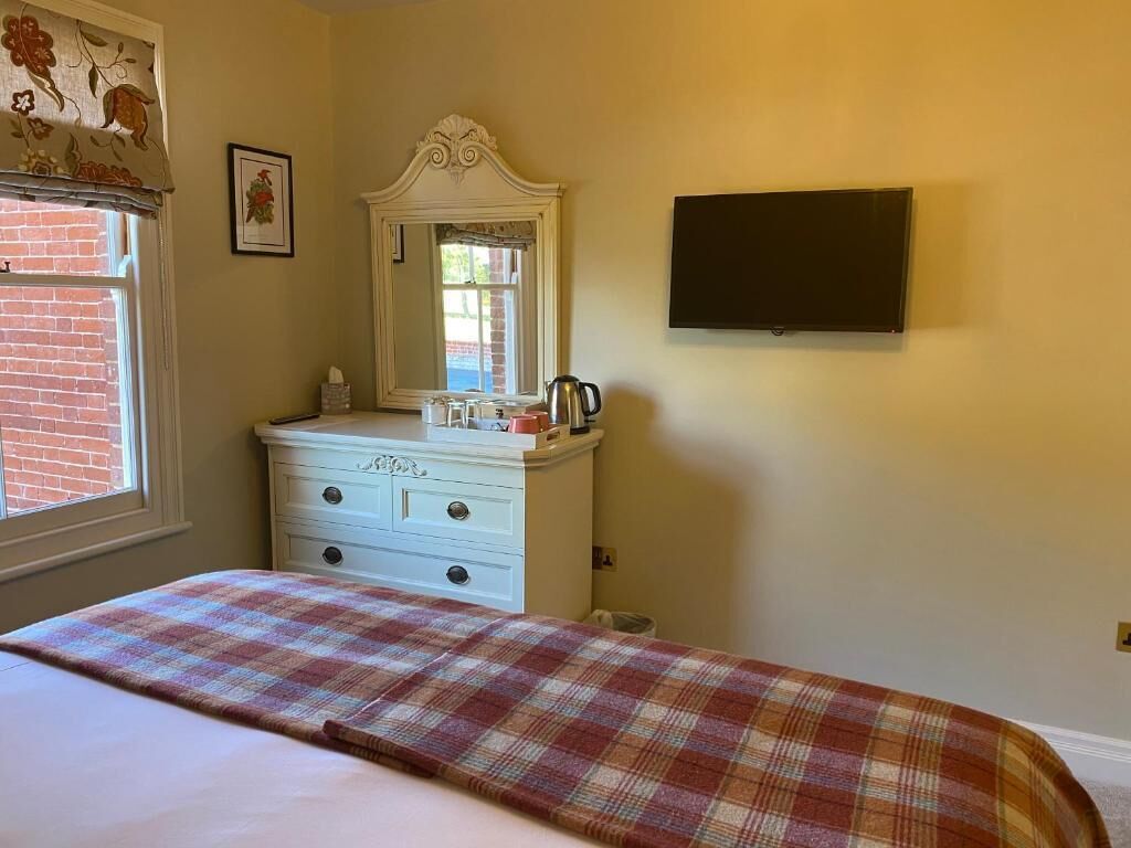 Un dormitorio con cama, cómoda, espejo, televisor de pantalla plana y ventana con vista a un edificio de ladrillo.