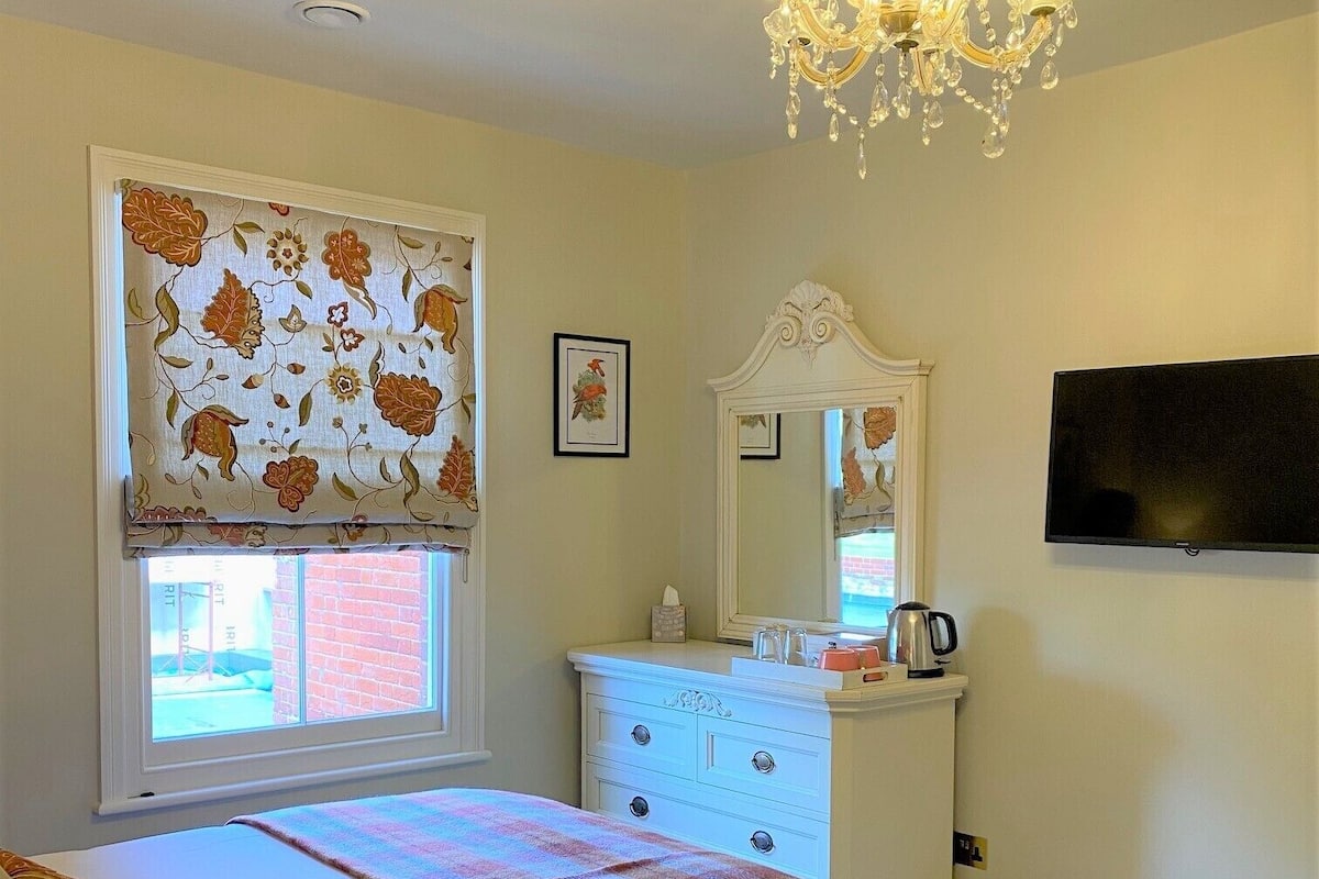 A bedroom with a bed, a dresser, a mirror, a television, and a chandelier.