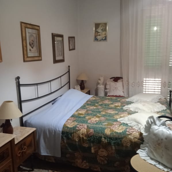 A bedroom with a bed, a nightstand, a lamp, a dresser, and a window with curtains.