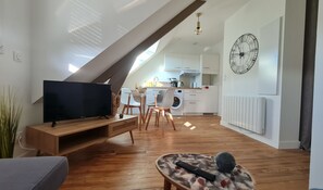 A modern apartment with a loft-style ceiling, a flat-screen TV, a dining area, and a kitchen.