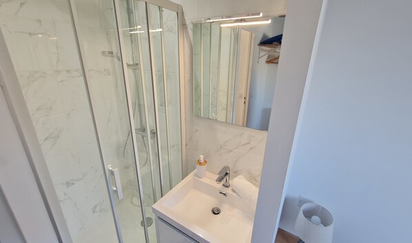 A modern bathroom with a glass-enclosed shower, a white sink, and a large mirror.